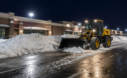 Snow removal equipment clearing a commercial parking lot at night